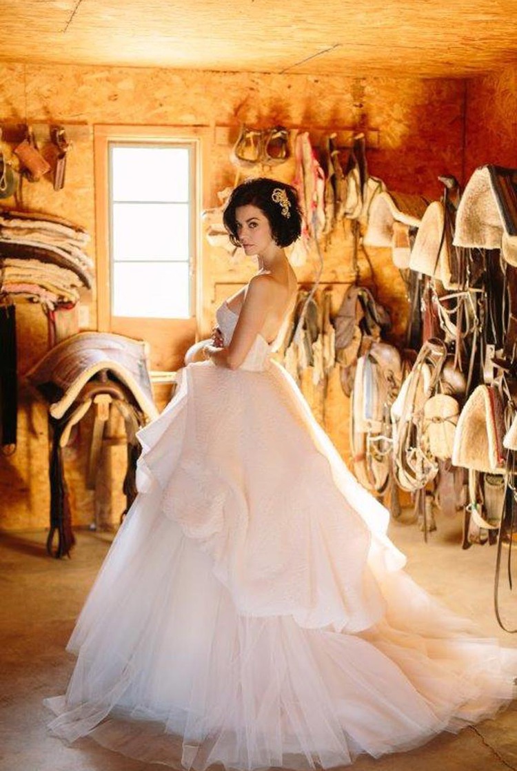 Bride standing in building with horse saddles hung on the wall