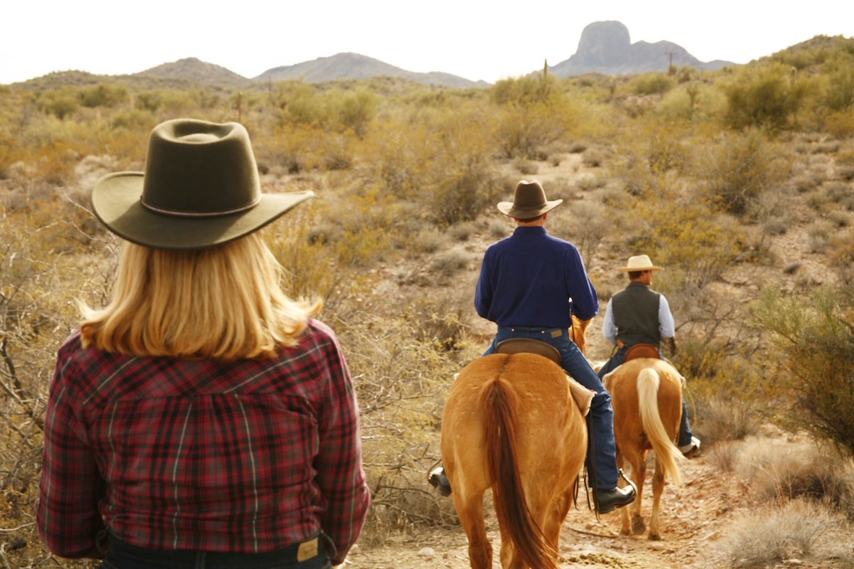 couple on horses with wrangler in the desert